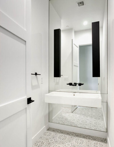 A bathroom designed and built by Armstrong Construction Group in Arizona. Features a full length mirror, a floating sink with black fixtures, and tile floor with ornate grey pattern.