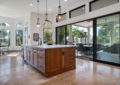 Custom kitchen designed and built by Armstrong Construction Group with a wood base island featuring a white countertop and hanging pendant lights above. Angle shows black sliding glass doors opening up onto the covered outdoor patio.