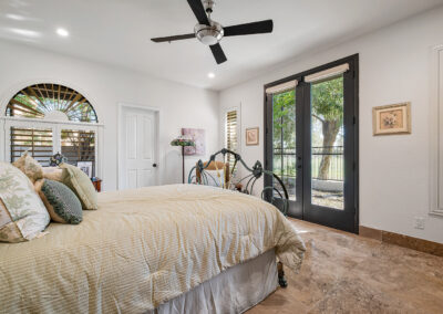 A bedroom designed and built by Armstrong Construction Group in Arizona. Room has white walls, black fench doors, brown marble floors, and lots of natural light.
